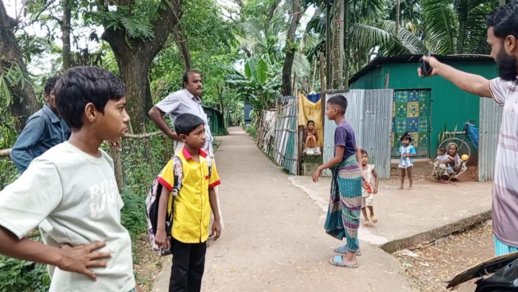 ফিতির মোল্লার বাড়ির সড়কের সরেজমিন পরিদর্শনের সময় স্থানীয় বাসিন্দা ও শিশুরা। যে স্থানে তারা দাঁড়িয়ে আছেন, সেখানে গাইড ওয়াল নির্মাণ হওয়ার কথা ছিল। স্থানীয়রা বলছেন কাজ হয়নি। এই কাজের ঠিকাদার তাহাসিন এন্টারপ্রাইজের স্বত্বাধিকারী রওশন আক্তার একেকবার একেক তথ্য দিচ্ছেন।